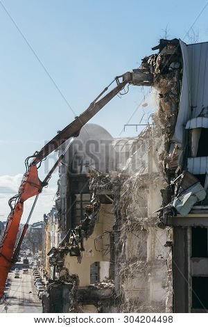 Excavator With Long Mechanical Arm At Height Breaks Off Pieces Of The House. Cleaning Area For A New