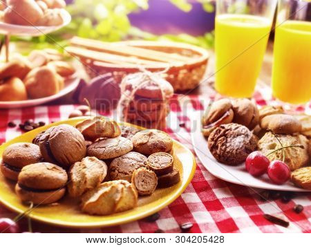 Chocolate oatmeal cookies and sand heart shape cake on plate table with fresh orange juice glass drink in country style. Rural table setting breakfast on gingham tablecloth.