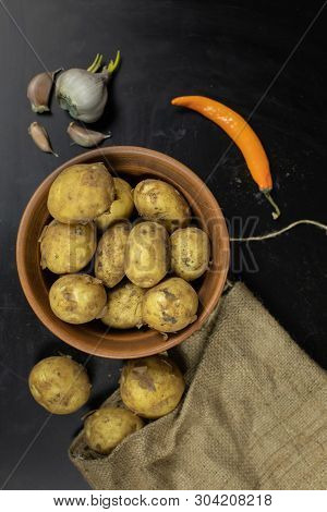 Potatoes On Black Surfase On A Plate. Fresh Potato With Traces Of Earth On The Skin. Dirty Raw Potat