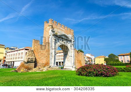 Ruins Of Ancient Brick Wall And Stone Gate Arch Of Augustus Arco Di Augusto, Green Lawn With Bush Of