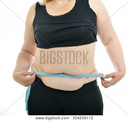 Overweight unhappy young woman measuring her waist, isolated over white background. Overeating xxl size woman with measuring tape