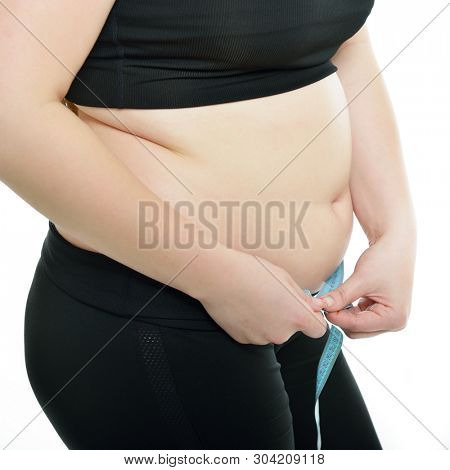 Overweight unhappy young woman measuring her waist, isolated over white background. Overeating xxl size woman with measuring tape
