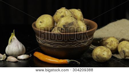 Potatoes On Black Surfase On A Plate. Fresh Potato With Traces Of Earth On The Skin. Dirty Raw Potat