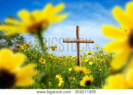 close up wooden cross on flower covered landscape over sunny blue sky