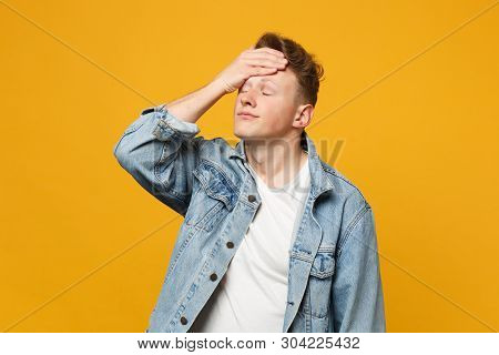 Portrait Of Tired Young Man In Denim Casual Clothes Keeping Eyes Closed, Putting Hand On Head Isolat