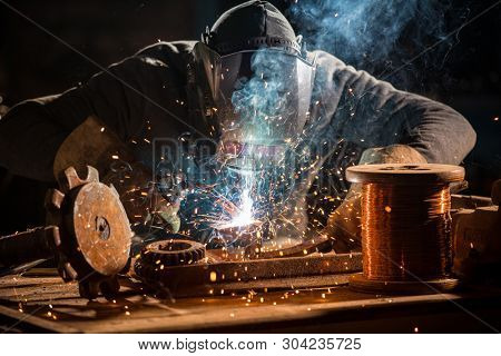 Welder is welding metal part in industrial workshop.