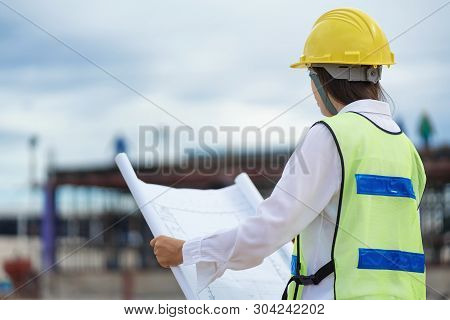 Woman Engineers Wear Safety Hats And Hold Blueprints And Radio Communications In Their Hands.
