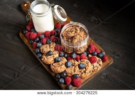 Diagonal Shot Of Homemade Cookies, Forest Fruits And A Milk Jar Over Wooden Platter