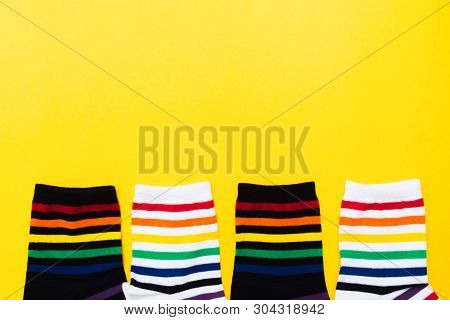 Four Black And White Socks With Colorful Striped Background Over Yellow Background With Copy Space. 
