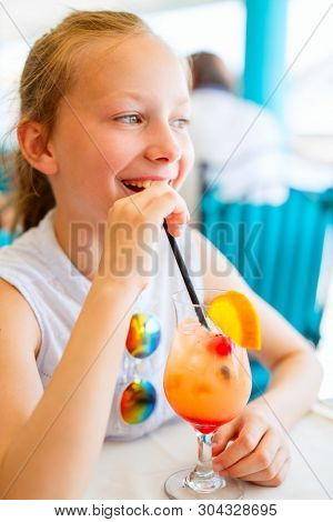 Adorable little girl drinking tropical juice mocktail at outdoor cafe on summer day