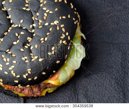 Black Hamburger On A Blue Background. Black Hamburger, Beef Cutlet, Pickled Gherkins, Lettuce Leaves