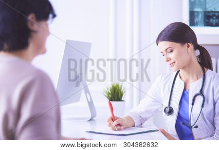 Doctor and patient discussing medical problems in a hospital consulting room. Doc filling in a patient's form