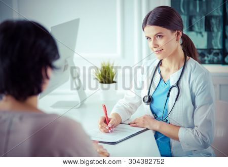 Doctor and patient discussing medical problems in a hospital consulting room. Doc filling in a patient's form