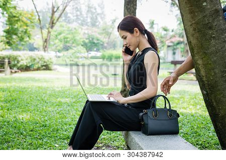 Hand Of Bandit Will Steal The Bag Behind The Woman, Who Sit And Using Smartphone And Laptop At The G