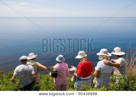Wanderer gehen zum Meer auf einer wilden Strecke am Hang des Berges. auf dem Meer ein Fischerboot.