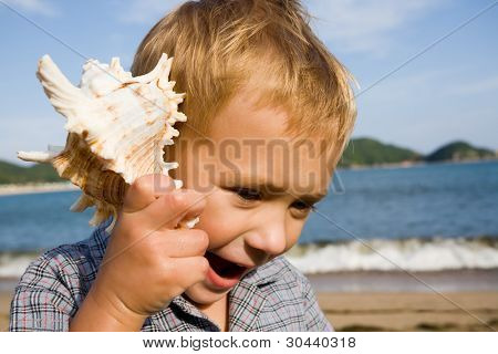 A kisfiú egy shell tartja a kezét.Tenger partján.