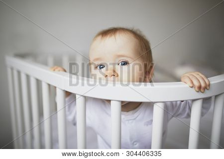 Adorable Baby Girl In Co-sleeper Crib Attached To Parents Bed. Little Kid Sitting In Cot