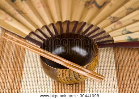 Dřevěná mísa (talíř), hůlky a ventilátor na bambusové rohoži.