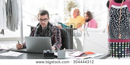 Designer Using Laptop And Graphics Tablet To Create Sketches Of New Clothes
