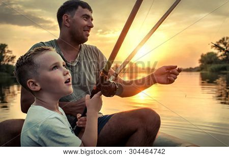 Happy Father and Son together fishing from a boat at sunset time in summer day under beautiful sky on the lake.
