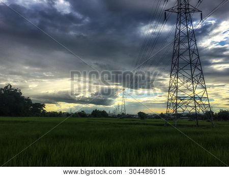 High Voltage Electric Power Pole Through The Rice Field In The Evening. Dark Cloud Adjust Like Paint