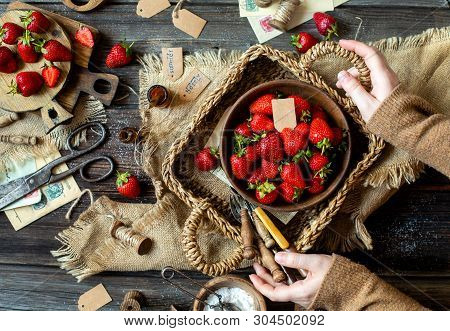 Overhead Shot Of Tasty Ripe Strawberries In Wooden Bowl Stands In Wicker Strawy Basket In Woman Hand