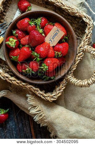 Overhead Shot Of Tasty Ripe Strawberries In Wooden Bowl Stands In Wicker Strawy Basket On Rustic Tab