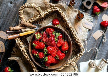 Overhead Shot Of Tasty Ripe Strawberries In Wooden Bowl Stands In Wicker Strawy Basket On Rustic Tab