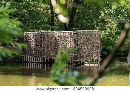 Wooden Building On The Shore Of The Pond. Wicker Building In The Forest.