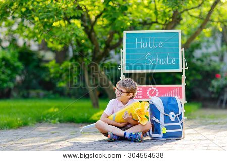 Happy Little Kid Boy With Glasses Sitting By Desk And Backpack Or Satchel