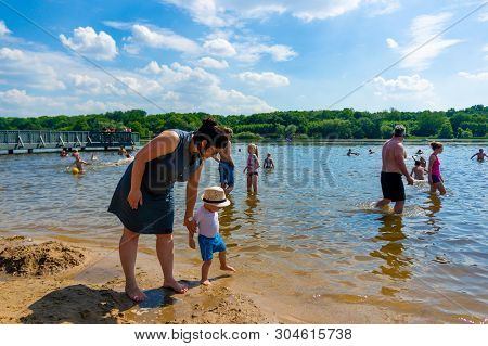 Woman And Small Child With Hat Walking Close By The Water At A Beach Of The Rusalka Lake On A Warm S