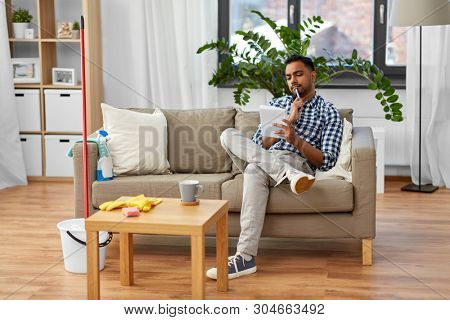 household and time management concept - indian man making to do list in notebook after home cleaning
