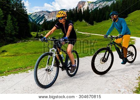 Cycling woman and man riding on bikes in Dolomites mountains andscape. Couple cycling MTB enduro trail track. Outdoor sport activity.
