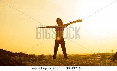 Young Woman Doing Stretching Outdoor. Warm up Exercise Against a Hot Beautiful Summer Sunset. Sport and Healthy Active Lifesyle Concept.