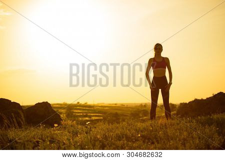 Young Woman Doing Stretching Outdoor. Warm up Exercise Against a Hot Beautiful Summer Sunset. Sport and Healthy Active Lifesyle Concept.