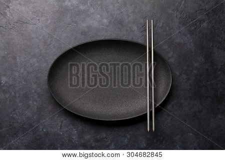 Empty plate and chopsticks over black textured table. Japanese food template. Top view with copy space. Flat lay