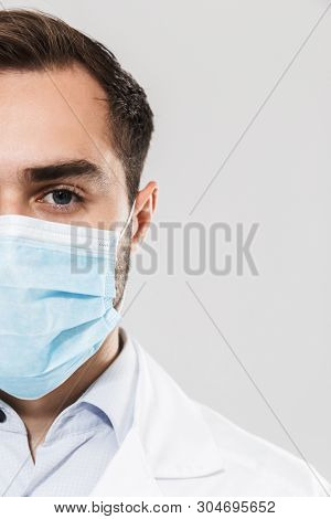 Portrait of brunette young medical doctor wearing sterile mask working in clinic laboratory and looking at camera isolated over white background
