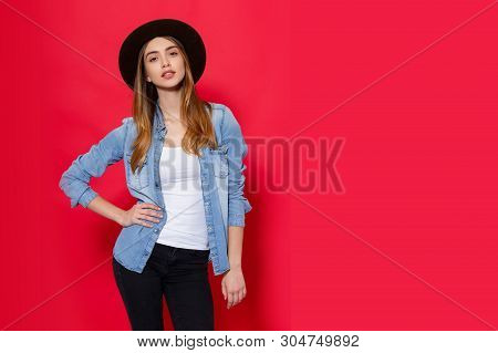 Cool Girl In Fashionable Outfit Poses With Attitudine In Studio On Red Bright Background. Place For 