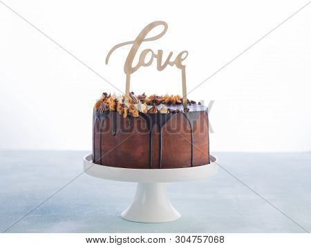 Wedding Cake With Melting Chocolate Ganache And Love Wood Caketopper On A White Background With Spac