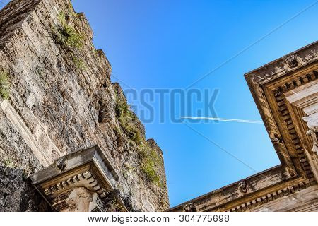 The Plane Leaving A Condensation Trail Flies High Above The Gates Of Hadrian. Adrian Gate, Antalya L