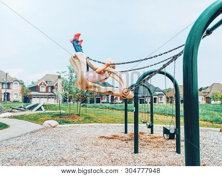 Little Preschool Girl In Tshirt And Jeans Swinging On Swings Very High Up In Air At Playground Outsi