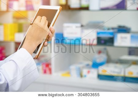 Pharmacist Working With A Tablet Computer In The Pharmacy Holding It In Her Hand While Reading Infor