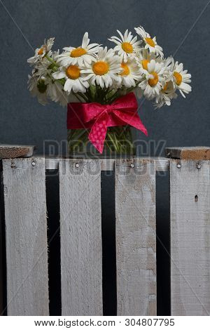 A Bouquet Of Field Daisies In A Glass Vase. On The  Wooden Box. Genus Of Perennial Flowering Plants