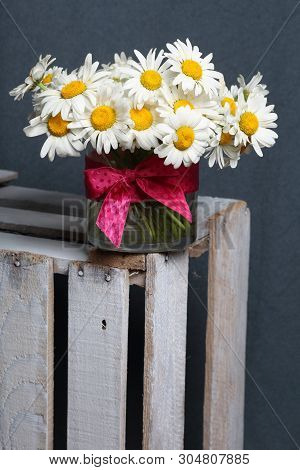 A Bouquet Of Field Daisies In A Glass Vase. On The  Wooden Box. Genus Of Perennial Flowering Plants