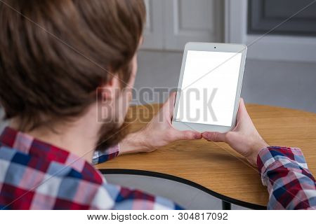 Man Sitting At Wooden Table And Looking At Digital Tablet Computer Device With White Blank Screen. M