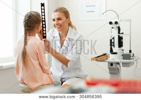 Blonde Caring Doctor Working With Little Girl While Observing Her Eyes