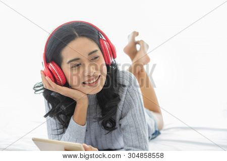 Close Up Shot Of Lovely Asian Woman Lie Prone, Prop Up, Smiles And Wearing Headphone That Connect To