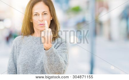 Beautiful middle age woman wearing winter sweater over isolated background Showing middle finger, impolite and rude fuck off expression