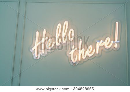 Neon glowing sign with word Hello there and green wall.