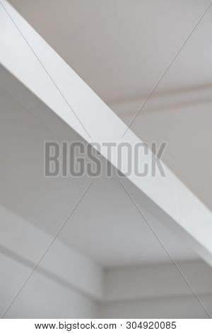 Features of a white room. A sides of a white wooden shelf in light and shadow.